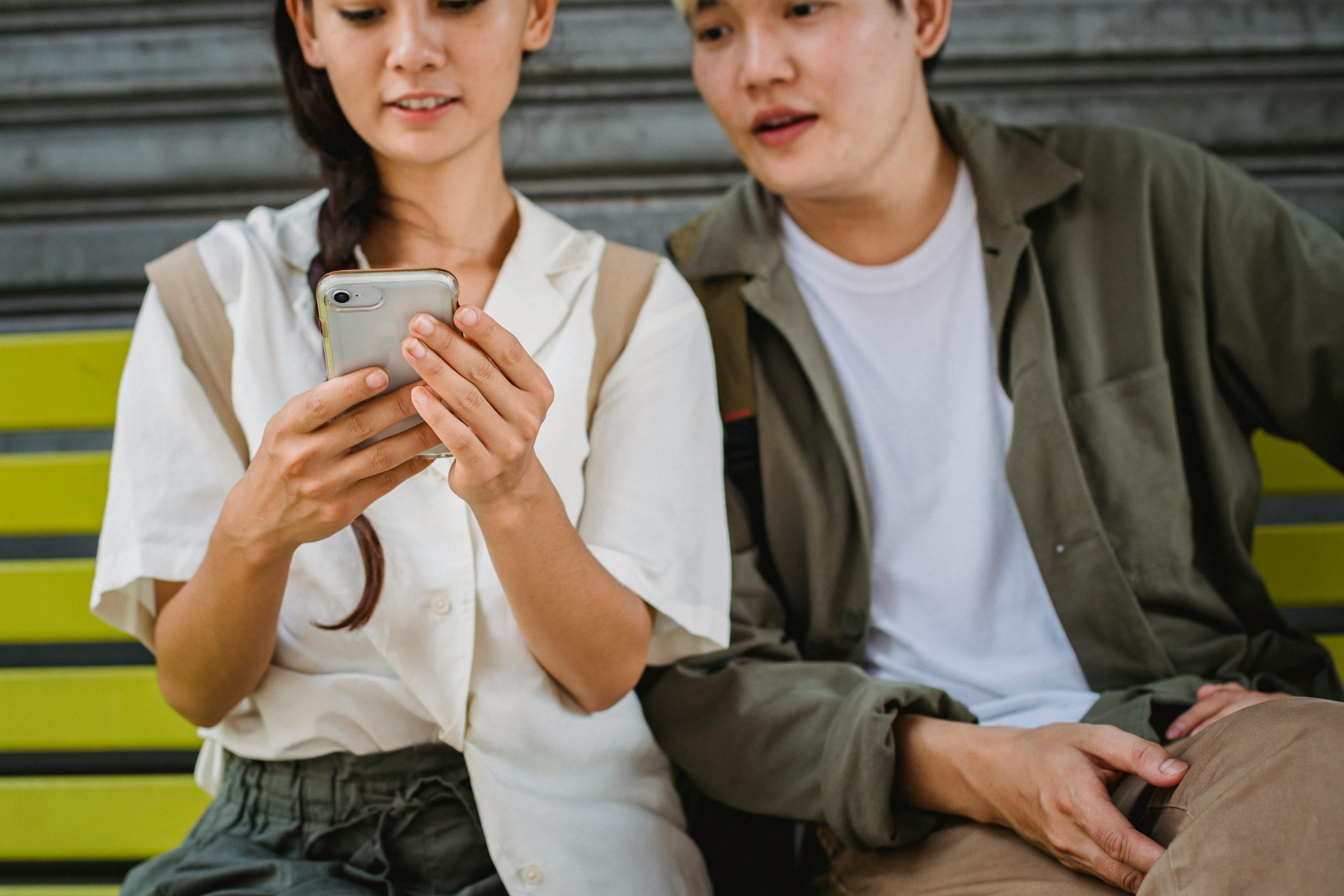 woman smiling while using her phone, with a man beside her glancing at the screen